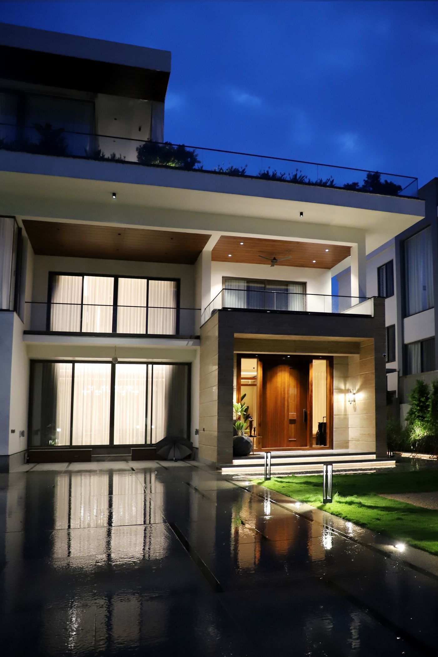 Two-story luxury villa glowing at dusk with landscaped entry